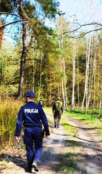 zdjęcie przedstawia policjanta w niebieskim mundurze, który idzie drogą polna i bierze udział w poszukiwaniach 53-letniego mężczyzny. Naokoło drogi jest las.